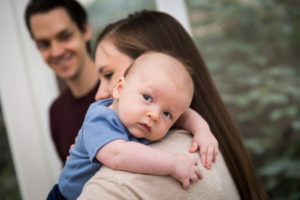 Mother holding newborn baby over shoulder for an article on how to prepare for a newborn portrait session