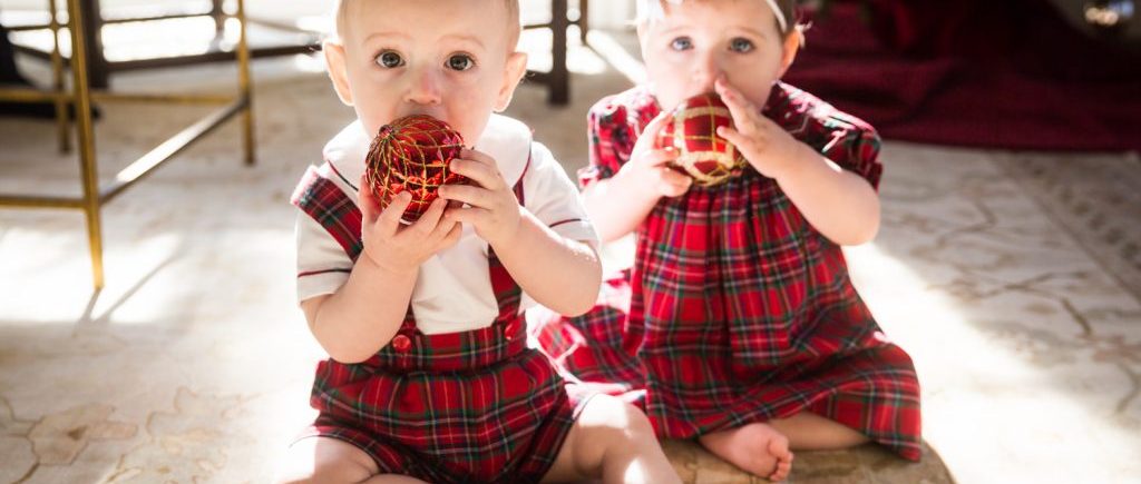 Two babies chewing on Christmas ornaments for an article on holiday family portrait ideas