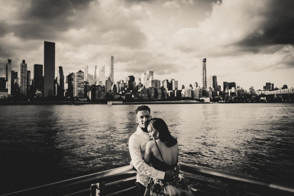 Black and white photo of engaged couple hugging in front of NYC skyline