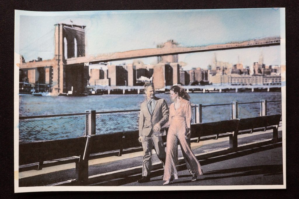 Hand-colored image of couple walking in front of Brooklyn Bridge