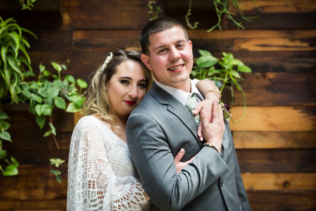 Brooklyn Winery wedding photos of bride and groom hugging in front of wall of plants