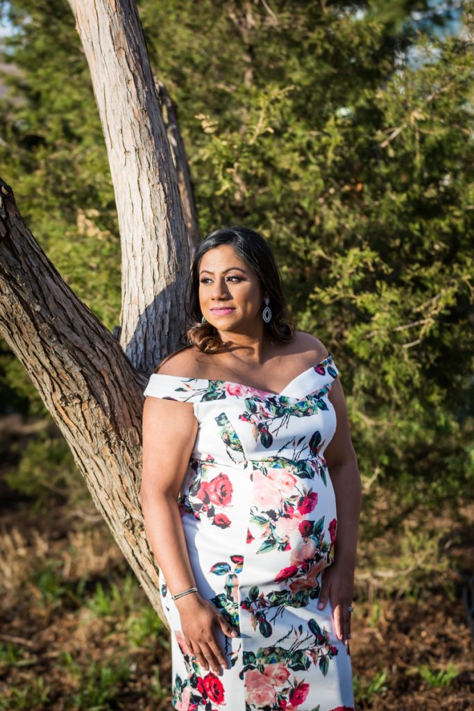 Pregnant woman wearing floral dress standing in front of tree