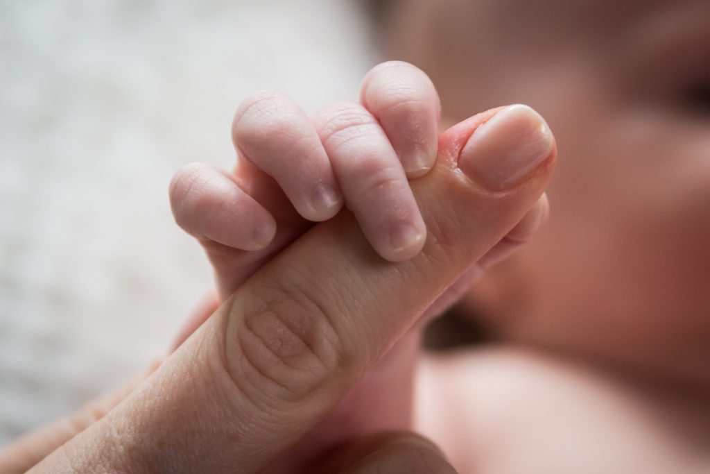 Close up of newborn baby holding on to mother's finger