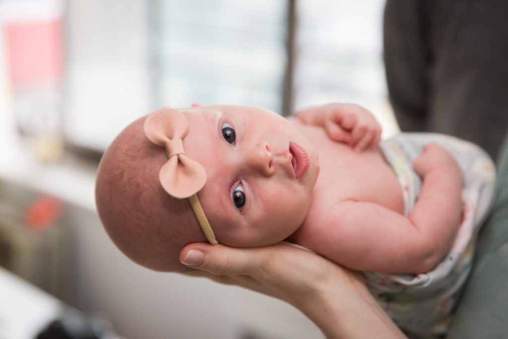 Newborn baby held on side and wearing bow in hair