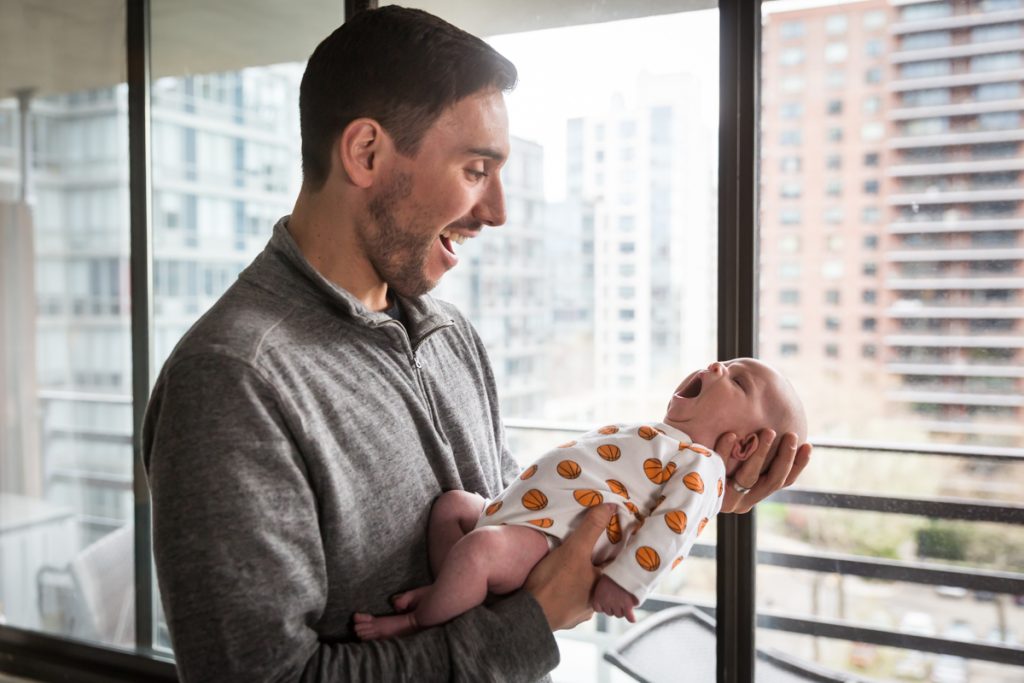 Father holding yawning newborn baby in front of window