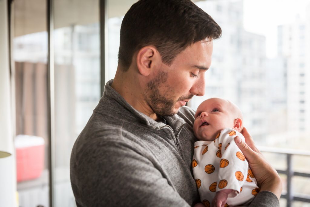 Father holding newborn baby in front of window
