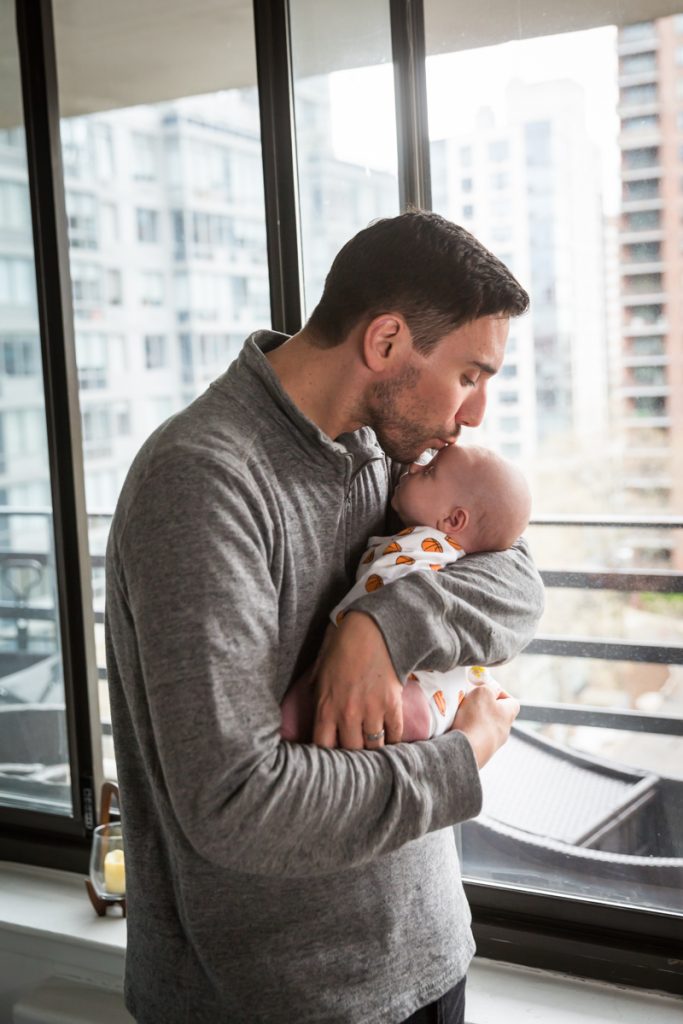 Father kissing newborn baby in front of window