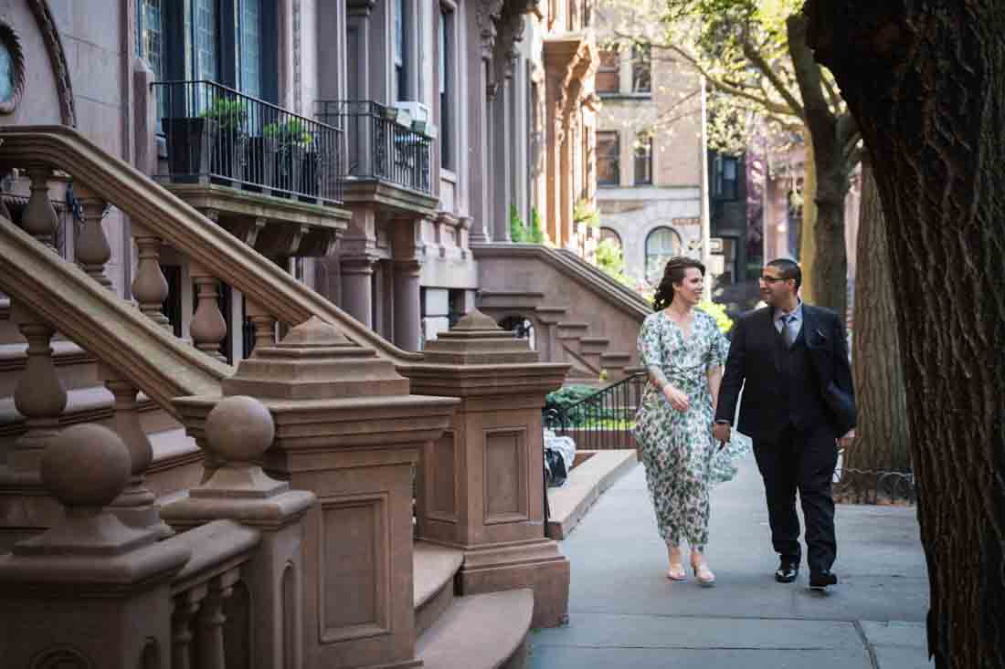Couple walking on sidewalk past brownstsones during a Brooklyn Heights Promenade engagement photo shoot