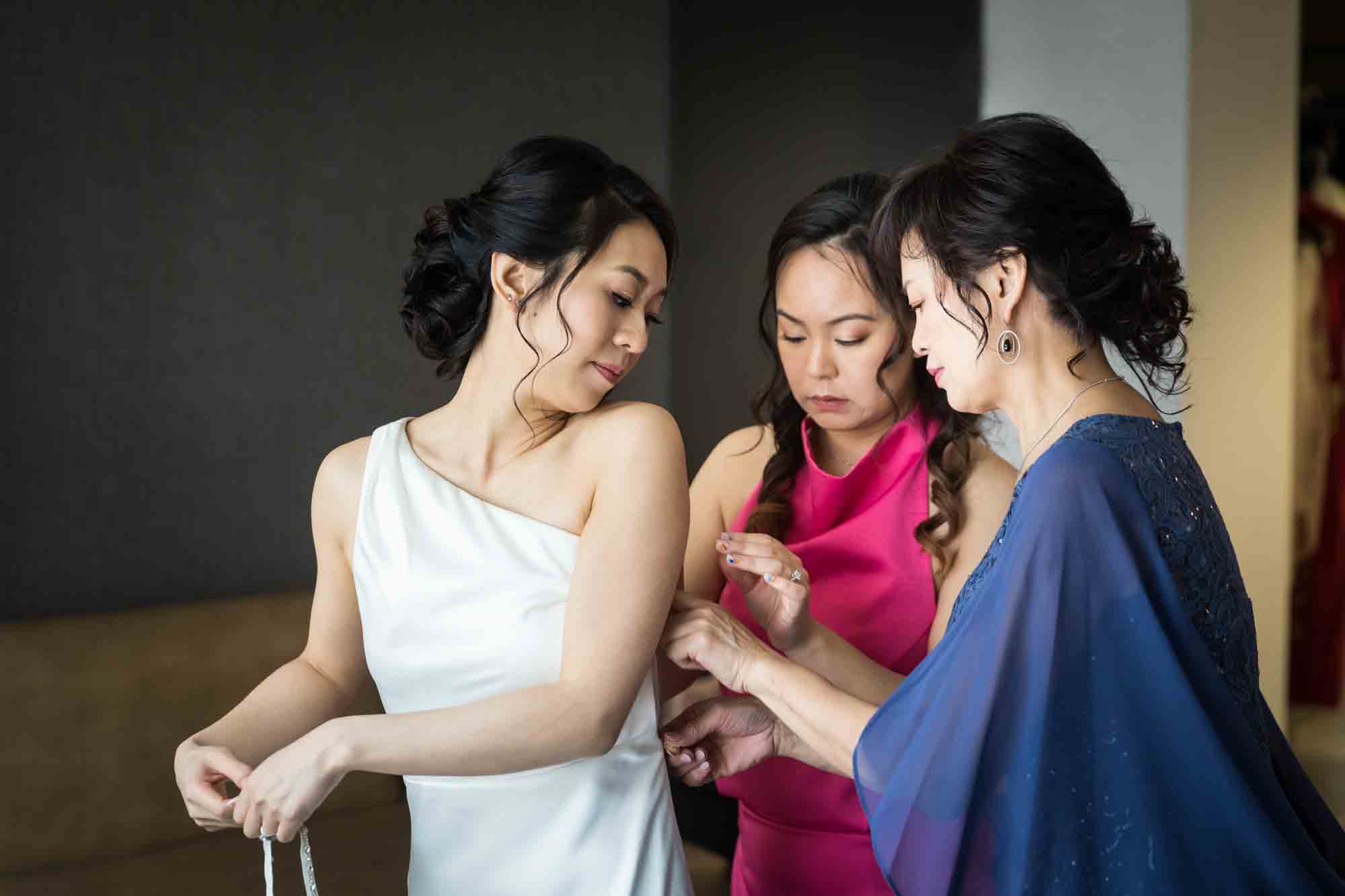 Mother and sister helping bride zip up dress
