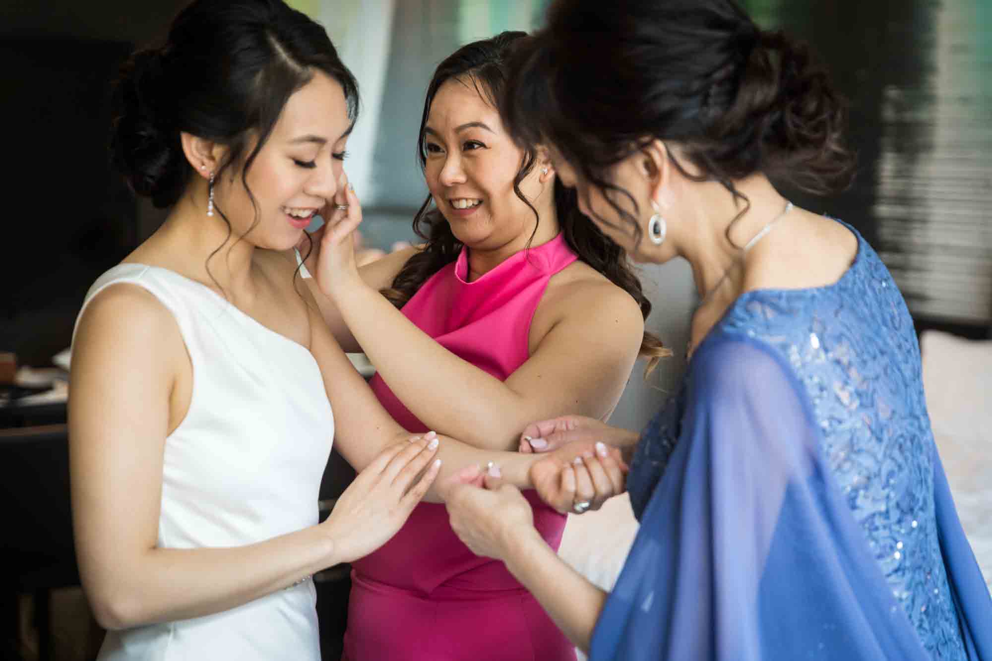 Mother and sister helping bride put on jewelry