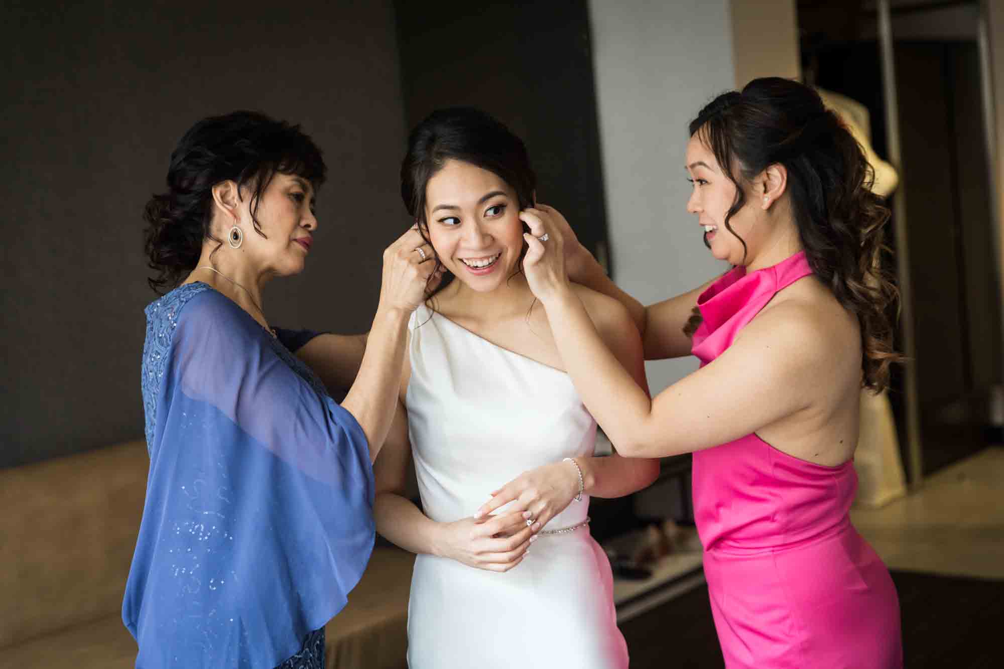 Mother and sister helping bride put on earrings