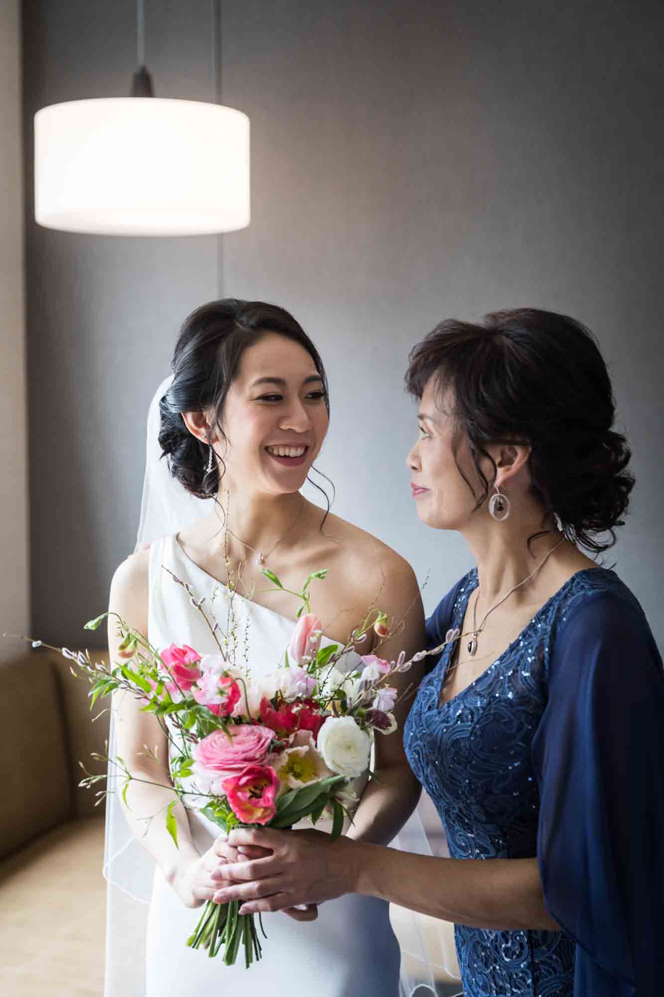 Mother and bride smiling at each other with bouquet