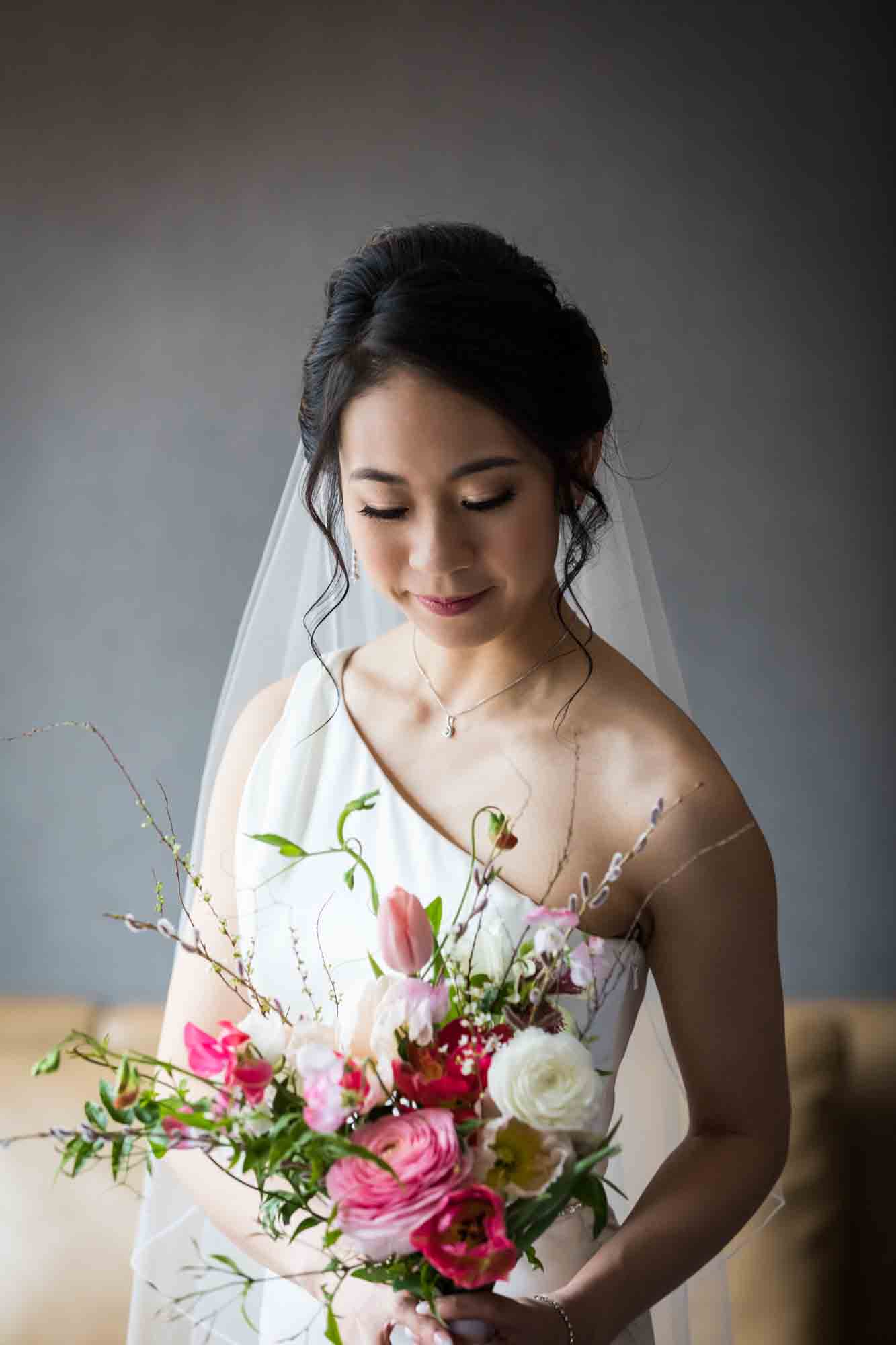 Bride looking down at flowers while wearing one-shoulder dress