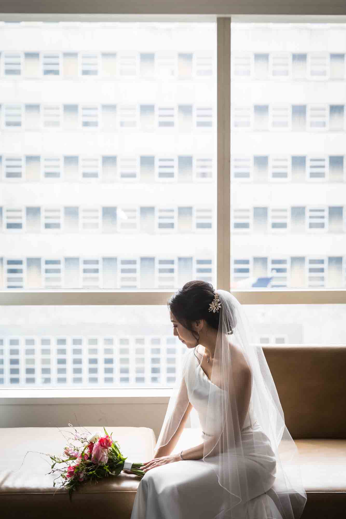 Bride sitting on couch with flowers and looking out window