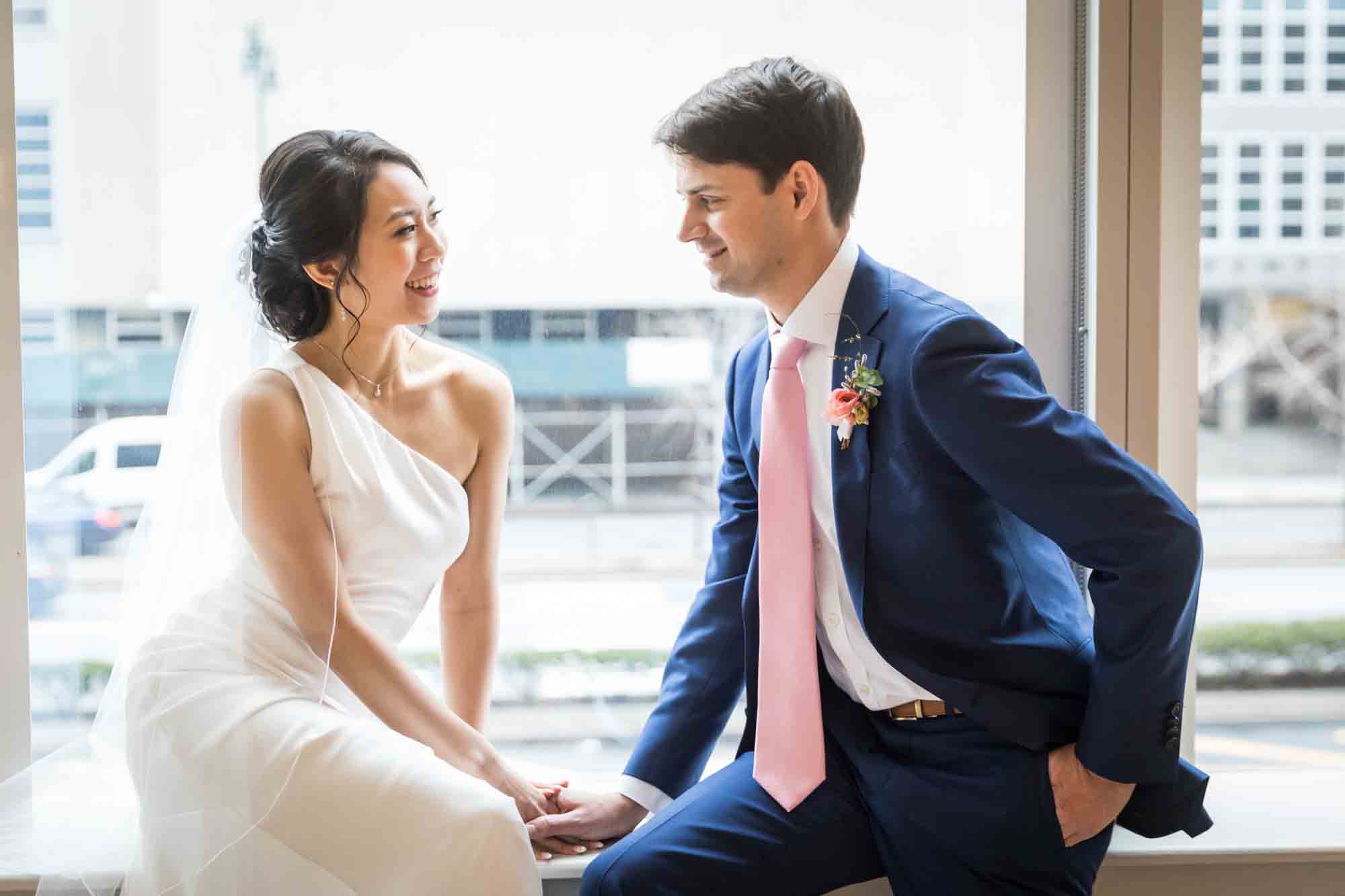 Bride and groom sitting in front of large window