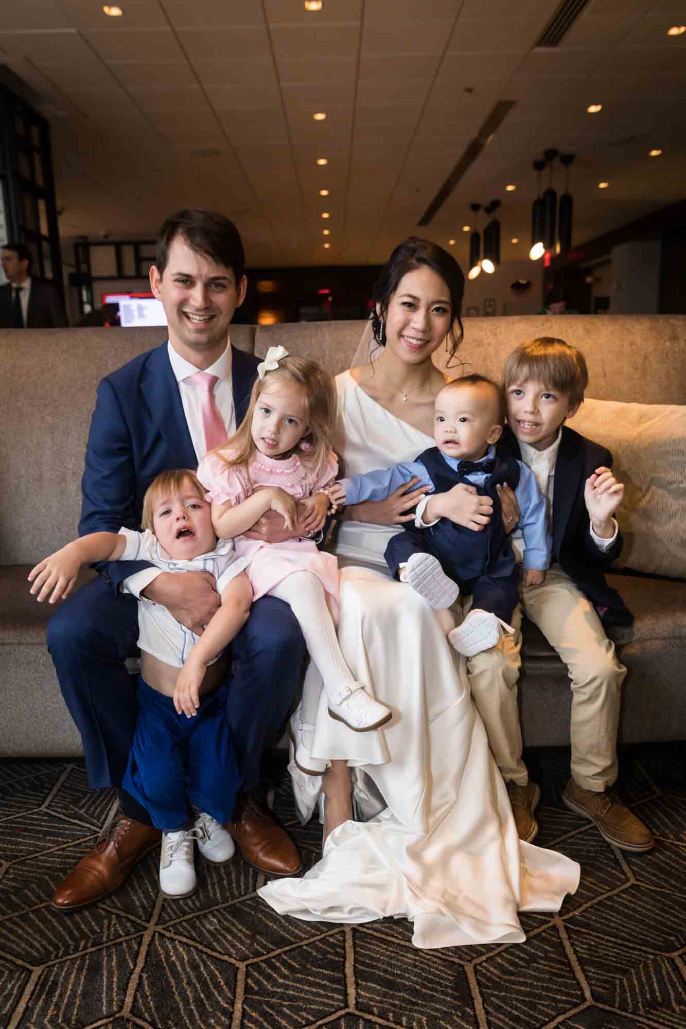 Bride and groom sitting on couch surrounded by children