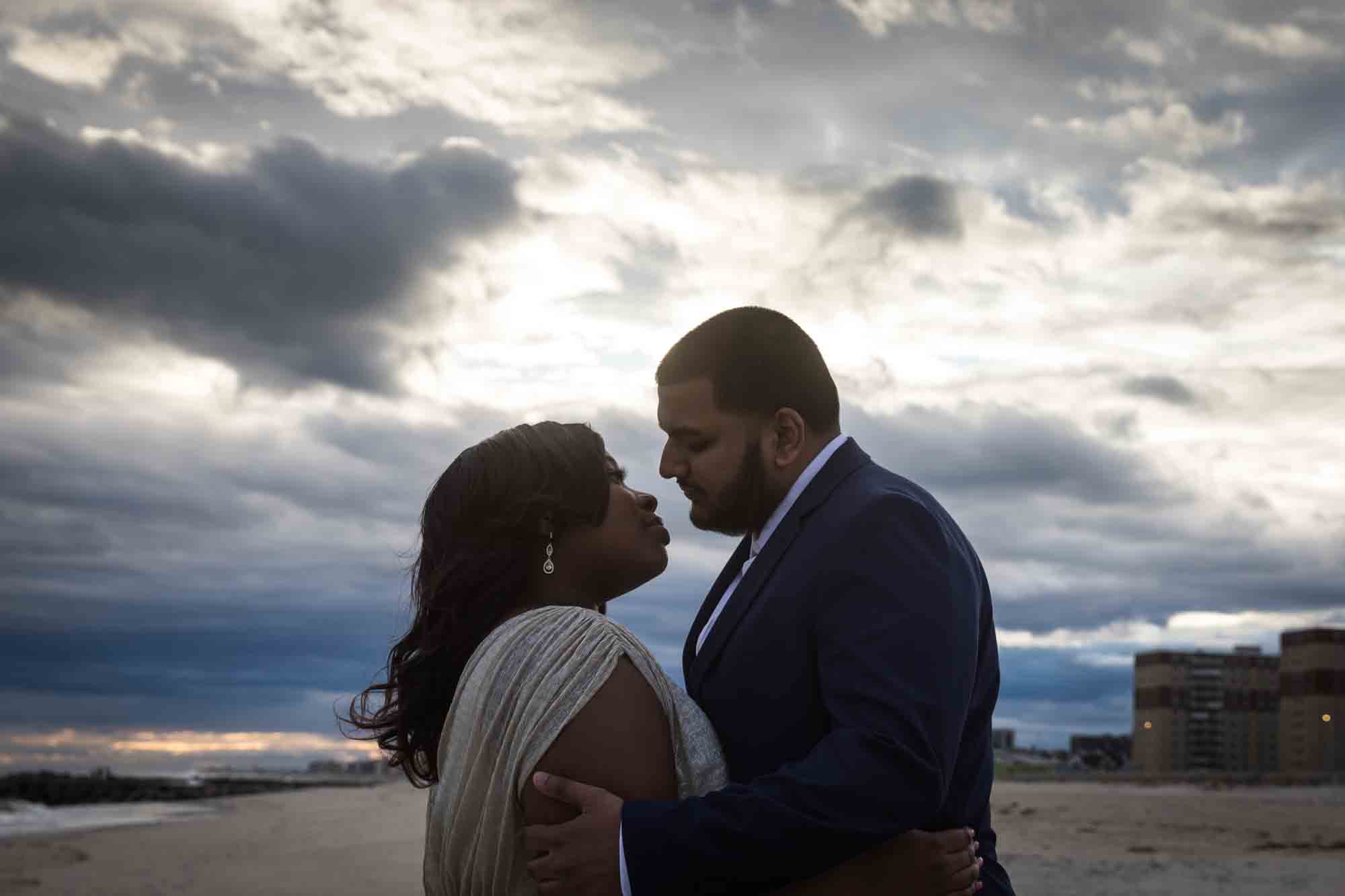 Couple about to kiss backlit against cloudy sky
