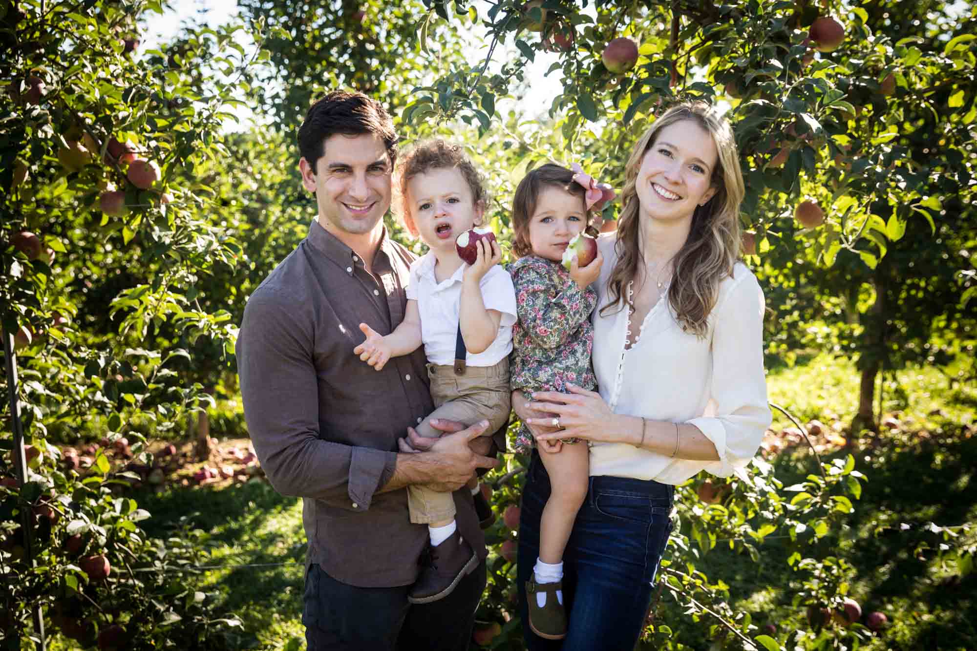 Parents holding toddlers in an orchard for an article on tips for apple picking family photos