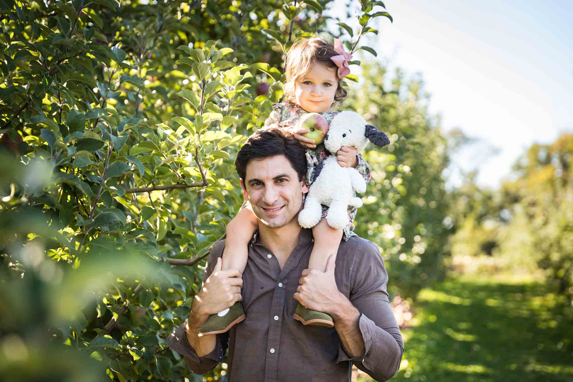 Father holding little girl on his shoulders in an orchard