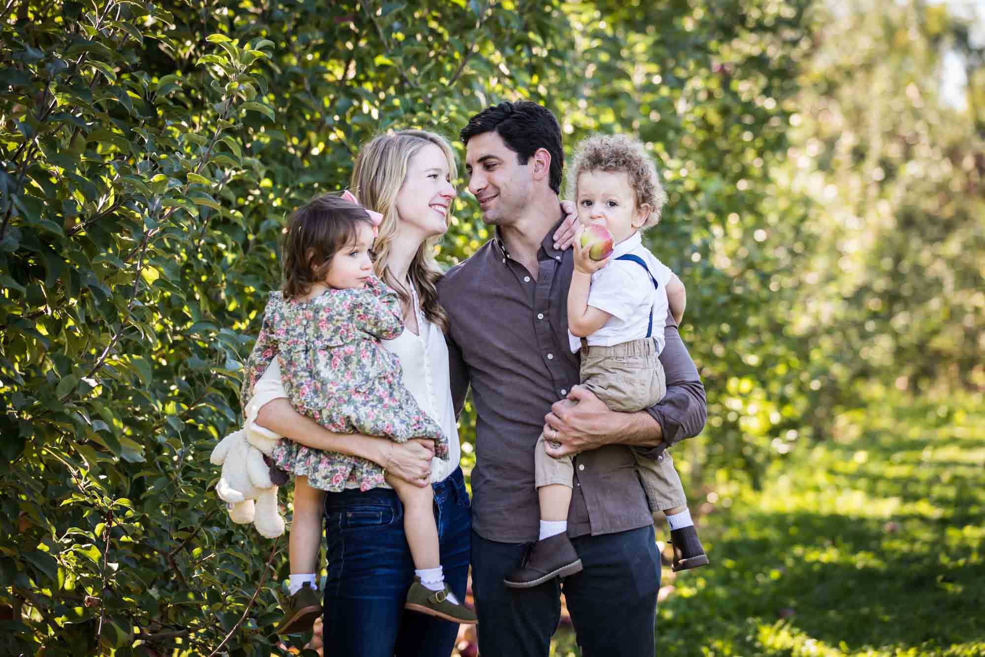 Parents holding little kids in apple orchard