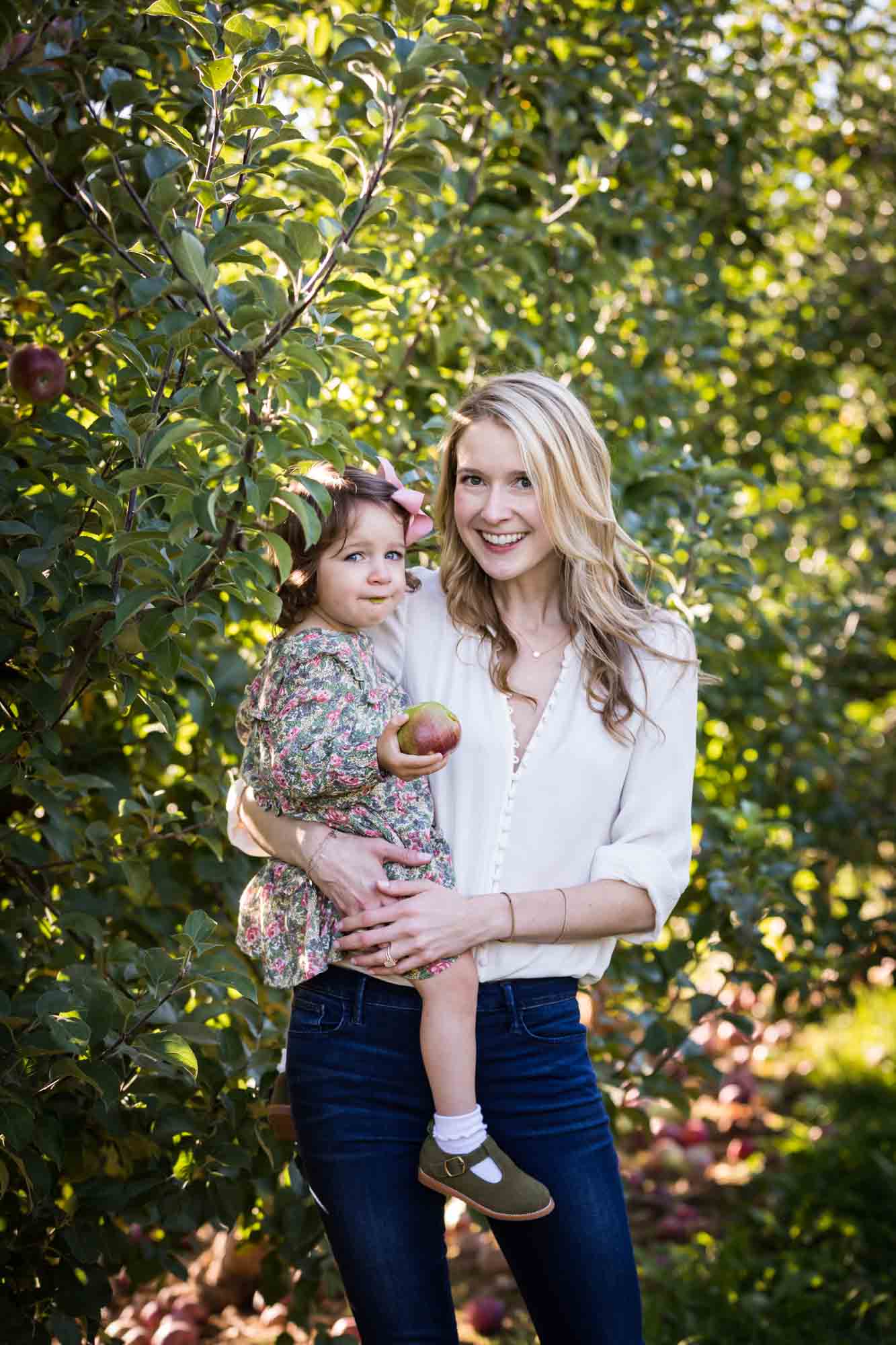 Mother holding little girl holding an apple for an article on tips for apple picking family photos
