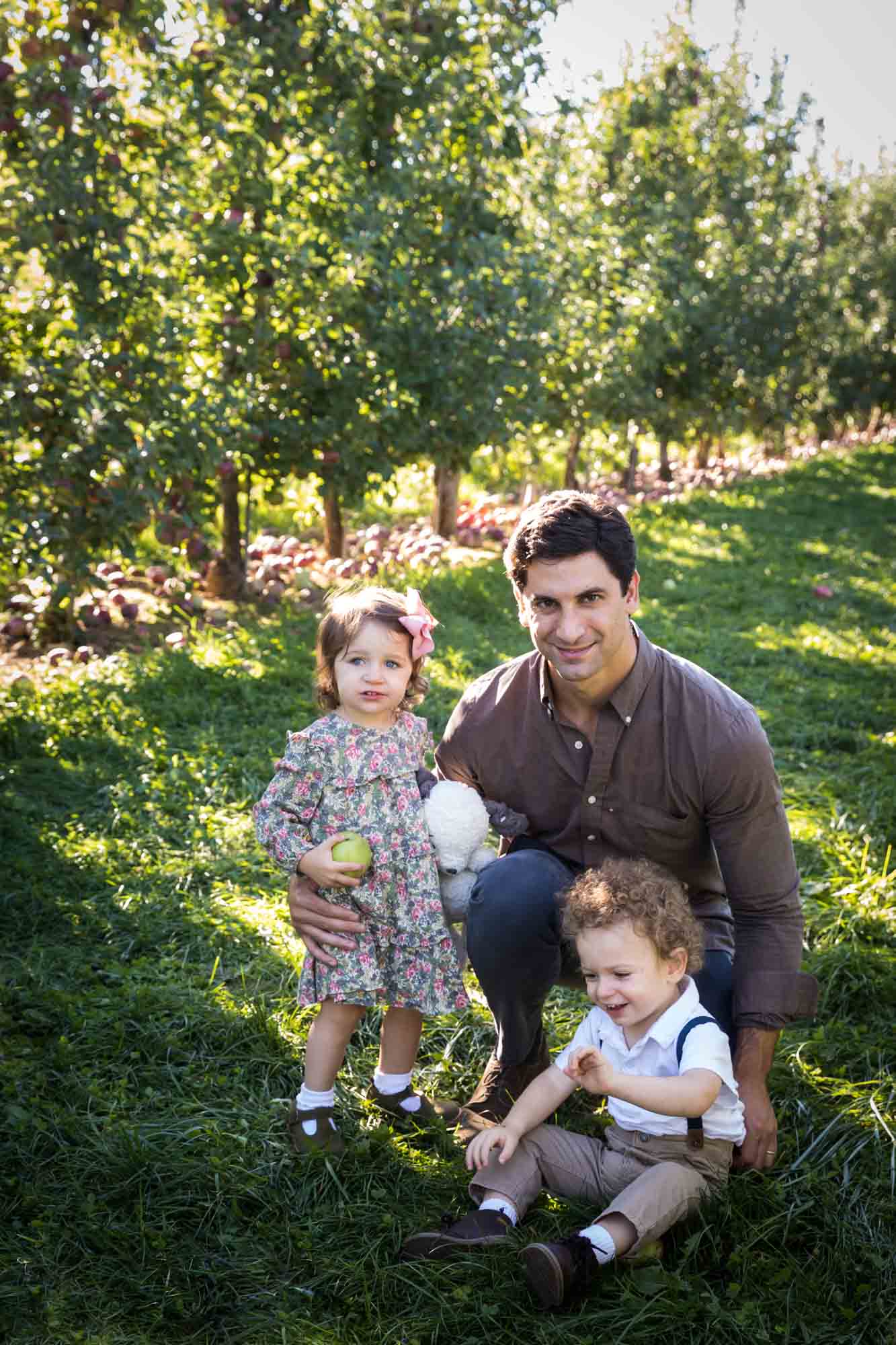Father with two toddlers in an orchard for an article on tips for apple picking family photos