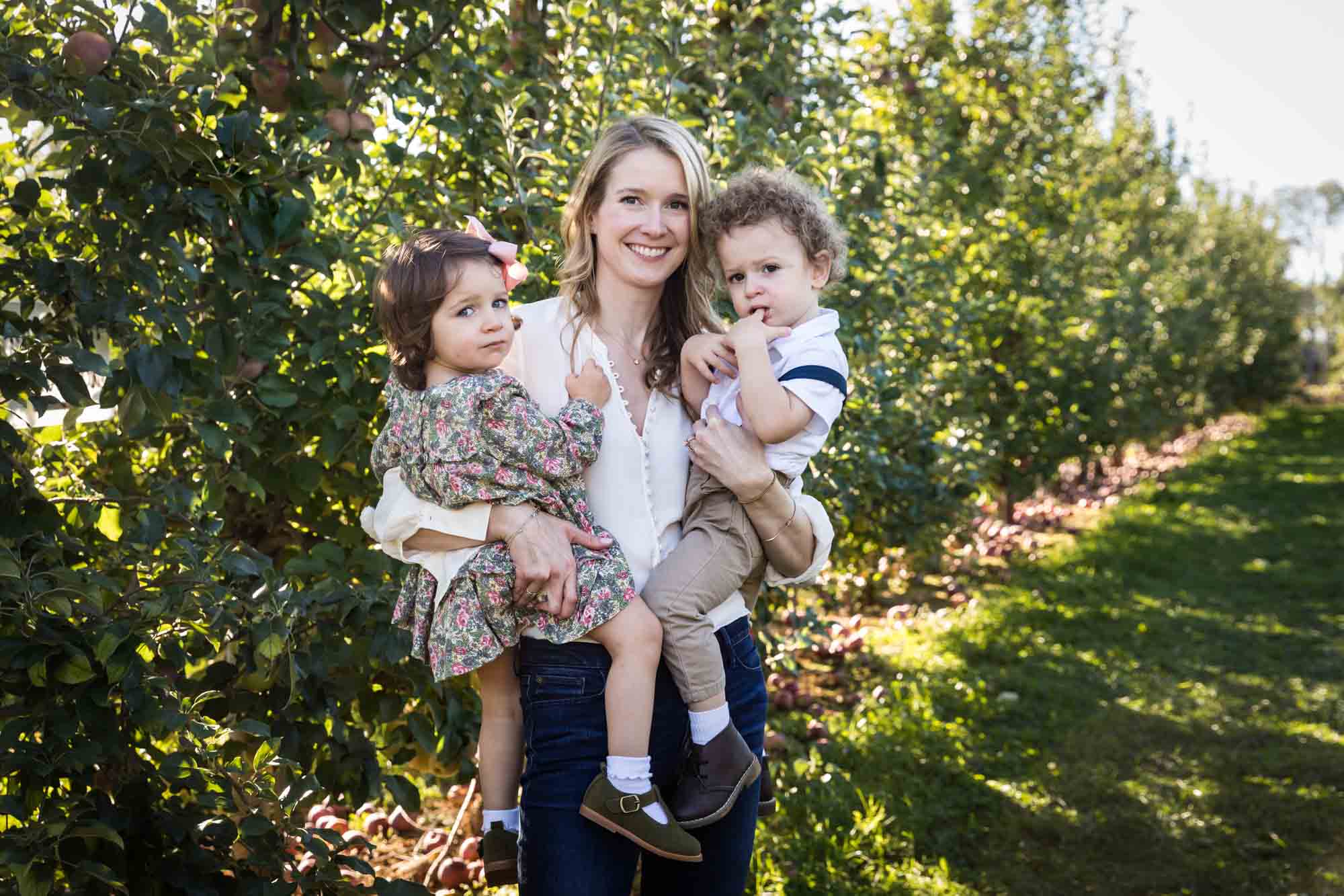 Mother holding two toddlers in orchard for an article on tips for apple picking family photos