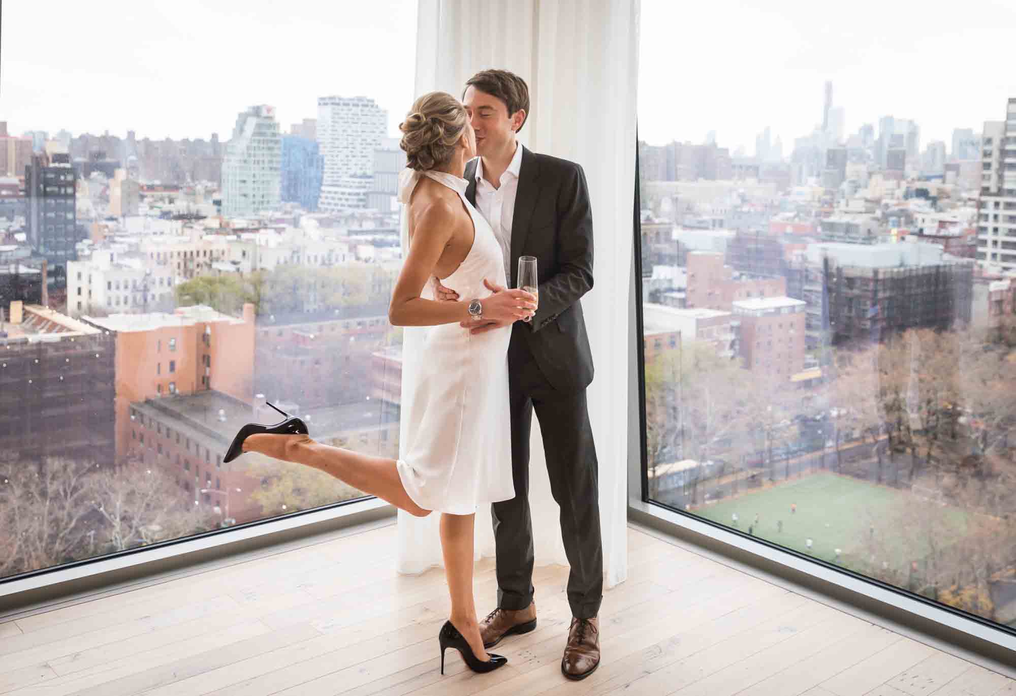 Bride and groom kissing in front of windows for an article on how to plan a hotel room wedding ceremony
