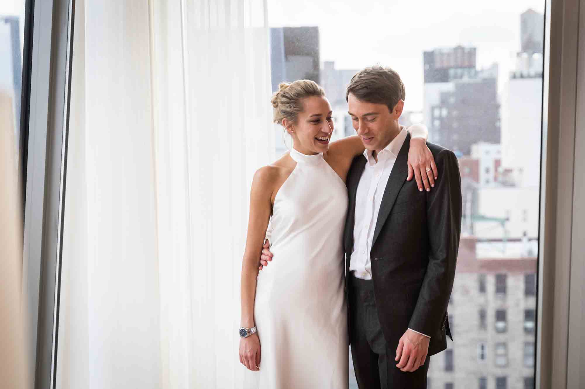 Couple hugging in front of white curtain before their Public Hotel wedding