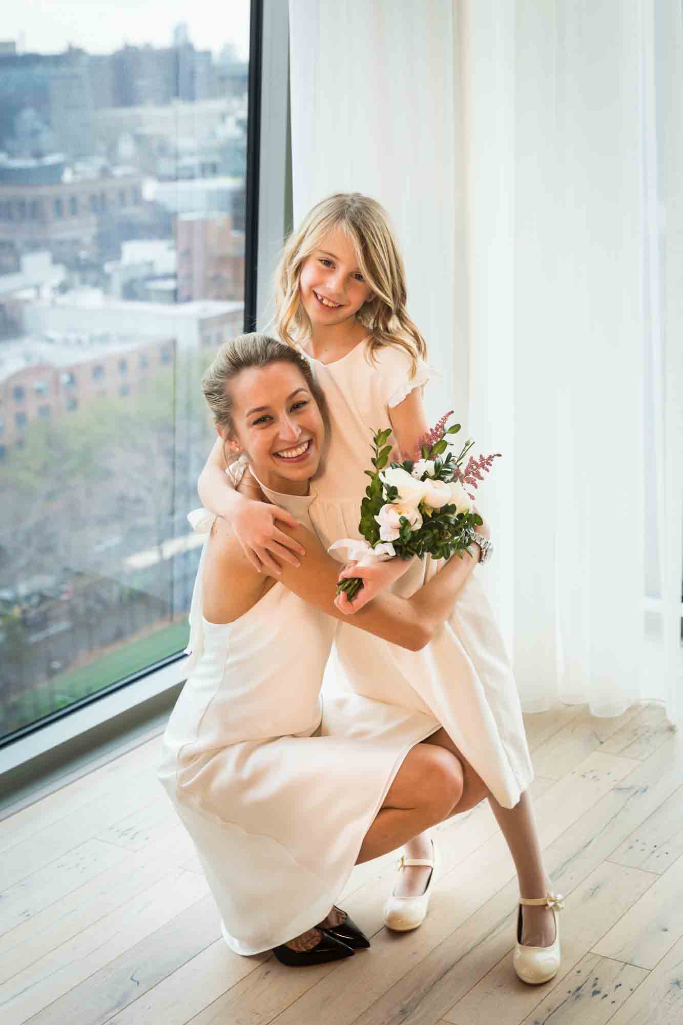 Bride hugging flower girl in front of window before a Public Hotel wedding