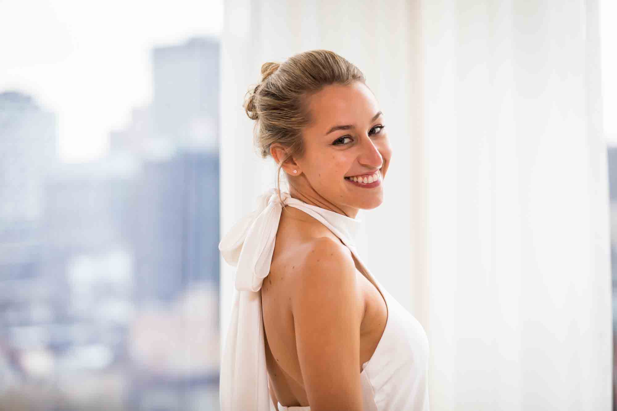 Smiling bride wearing sleeveless dress with hair up in front of white curtain