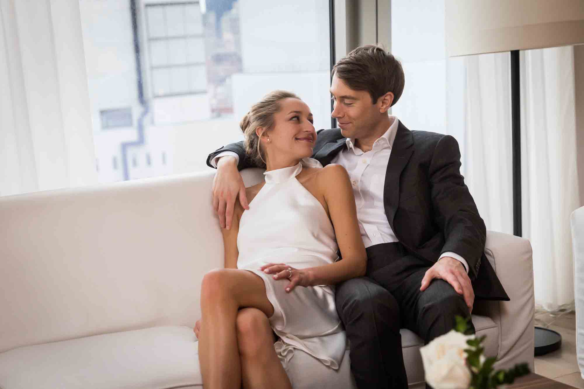 Couple sitting together on white couch for an article on how to plan a hotel room wedding ceremony