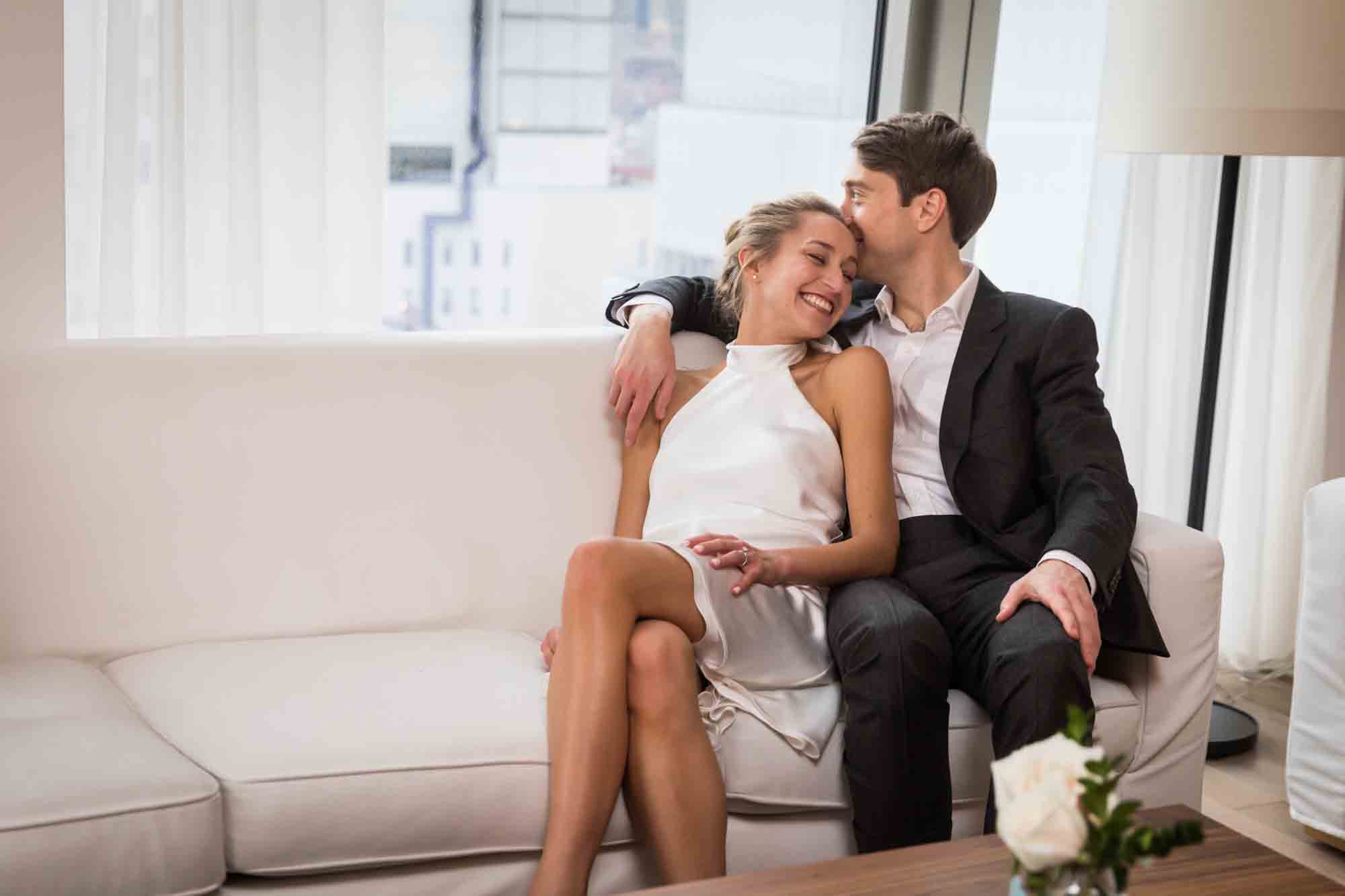 Couple sitting together on white couch for an article on how to plan a hotel room wedding ceremony