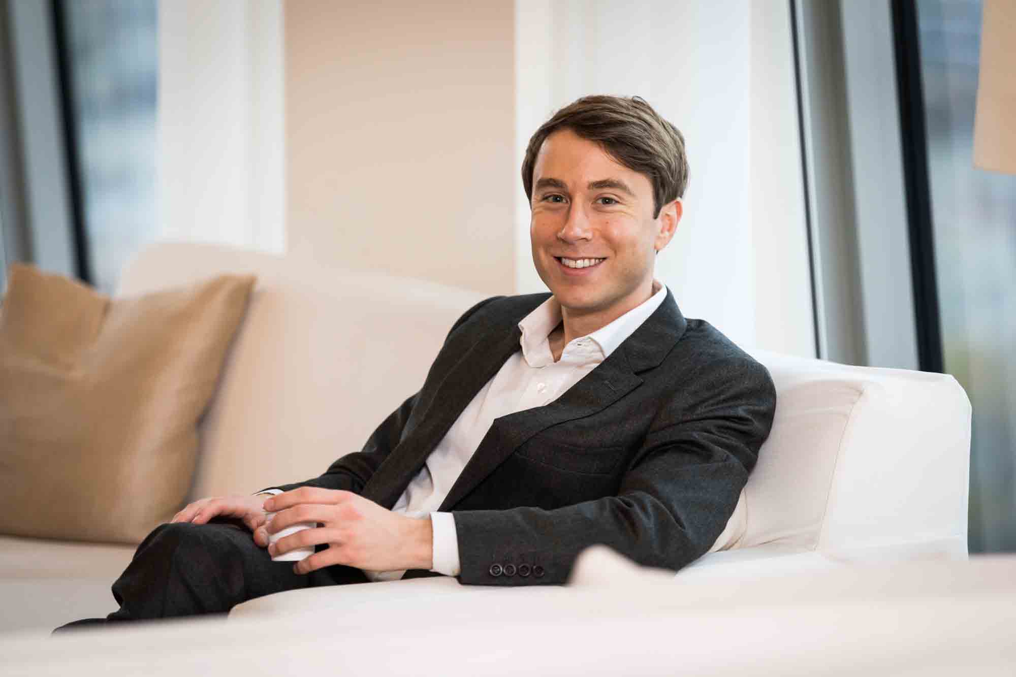 Groom sitting on white couch for an article on how to plan a hotel room wedding ceremony