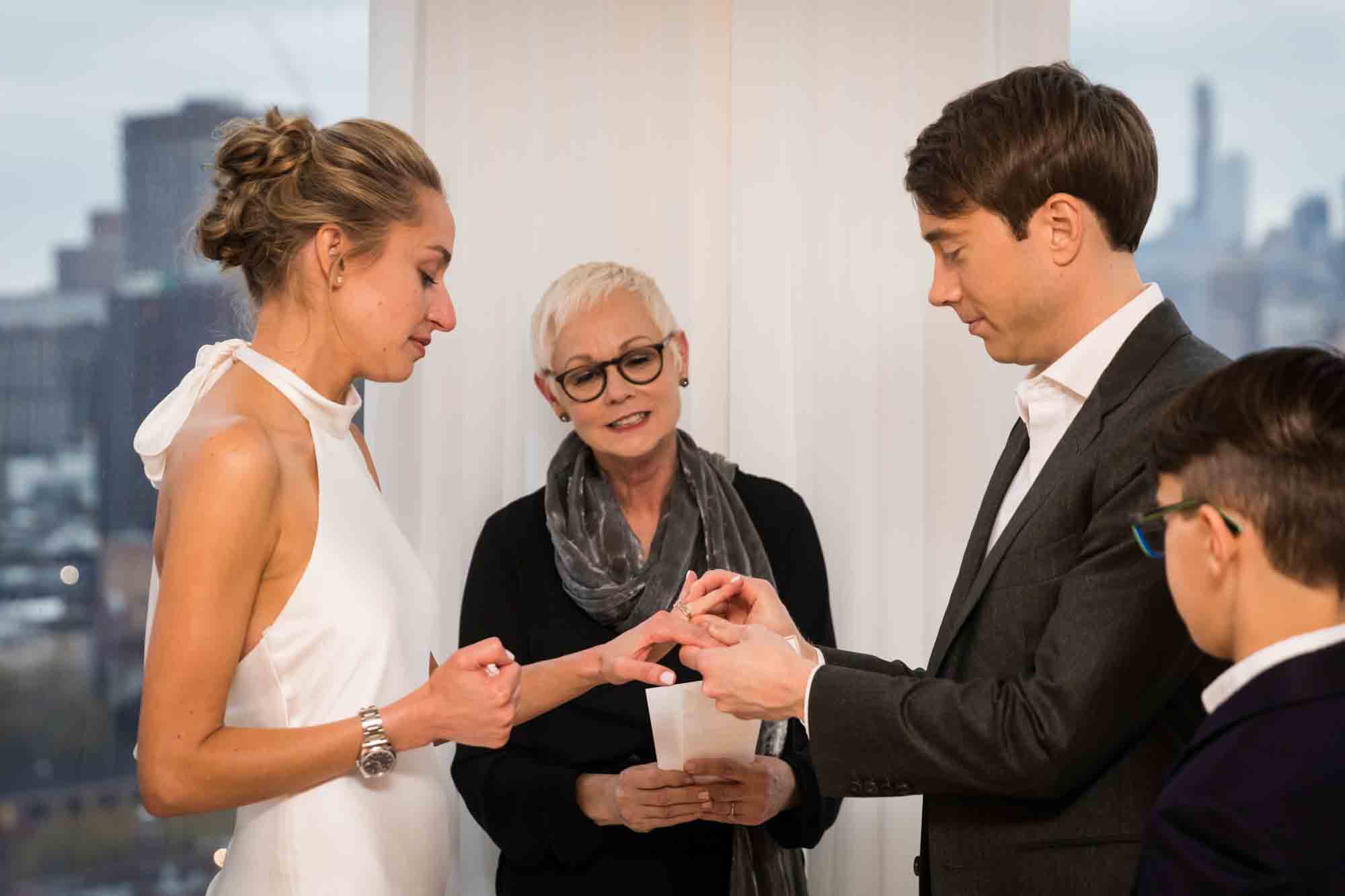 Officiant watching as groom puts ring on bride's finger