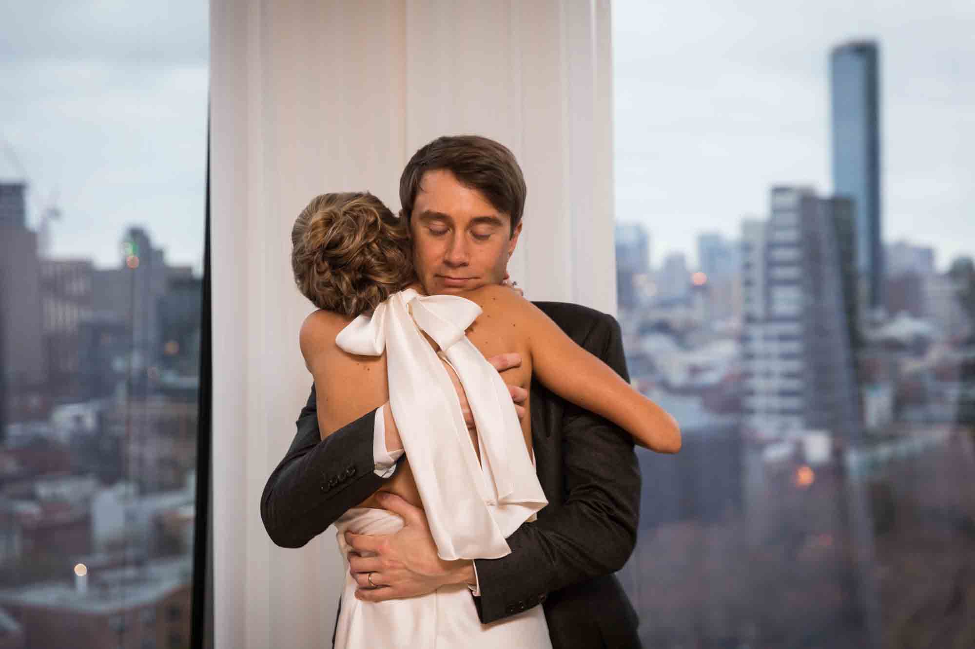 Groom hugging bride in front of windows at a Public Hotel wedding