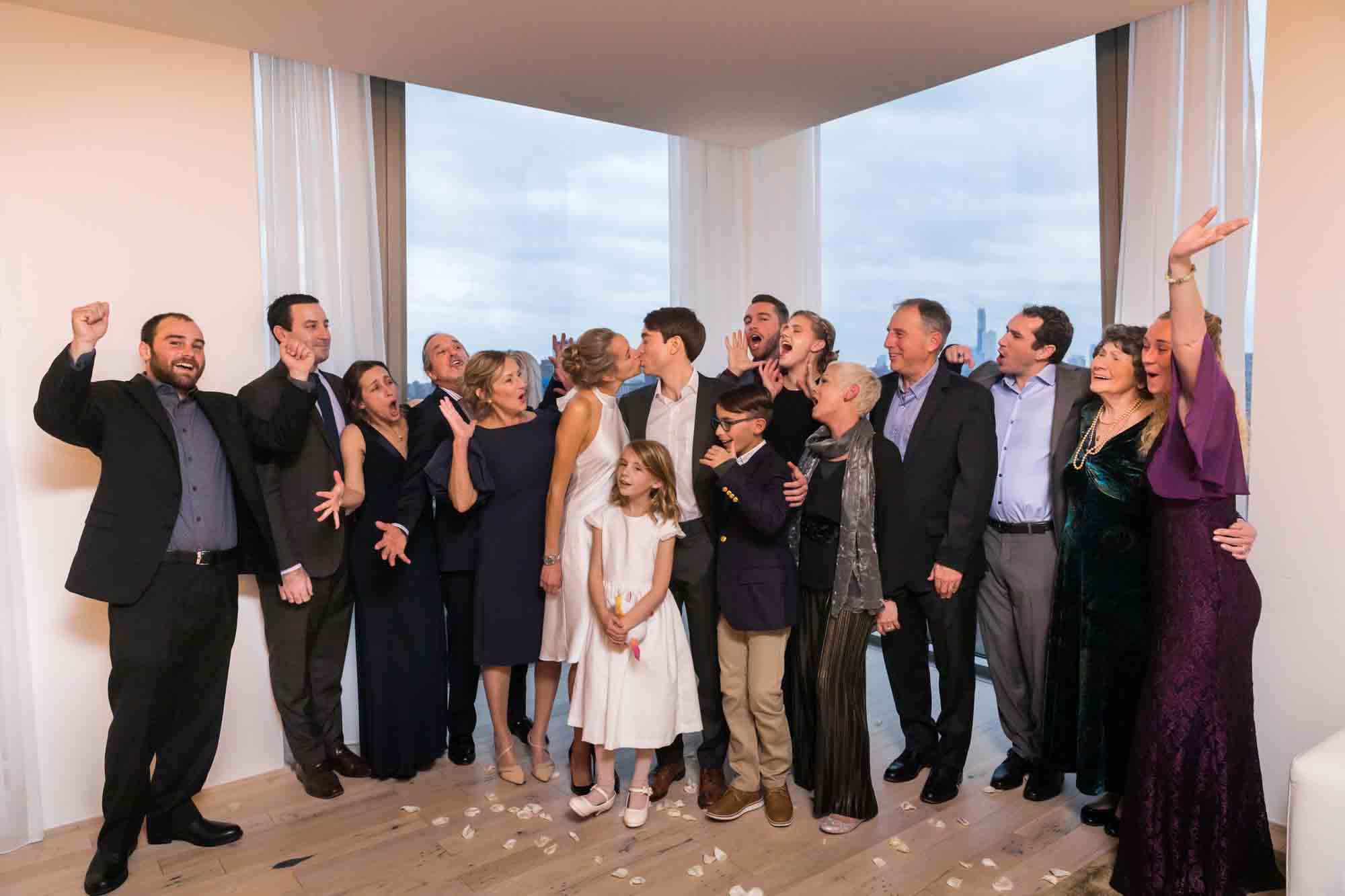 Family portrait with guests cheering as bride and groom kiss