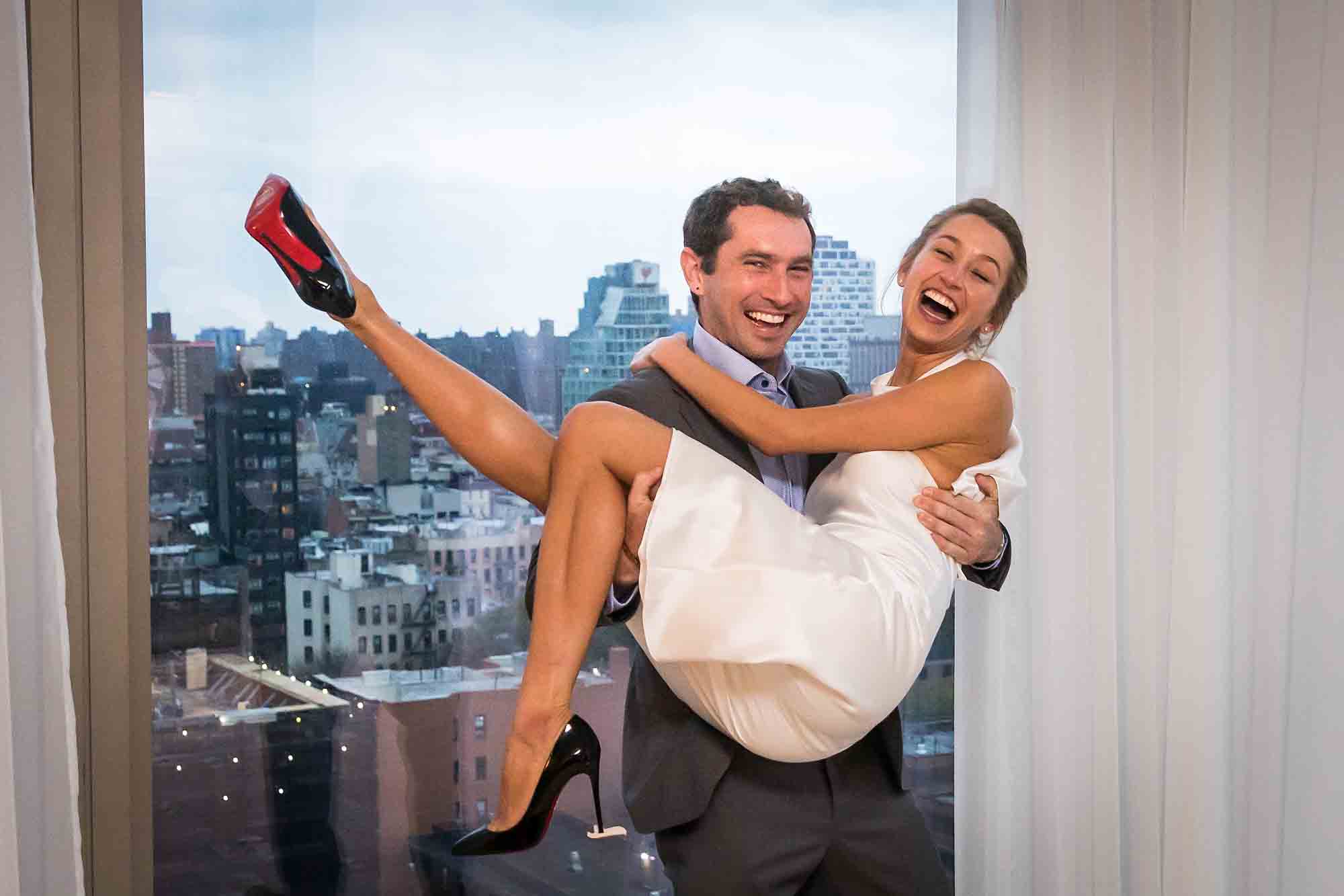 Male guest lifting up bride in front of window