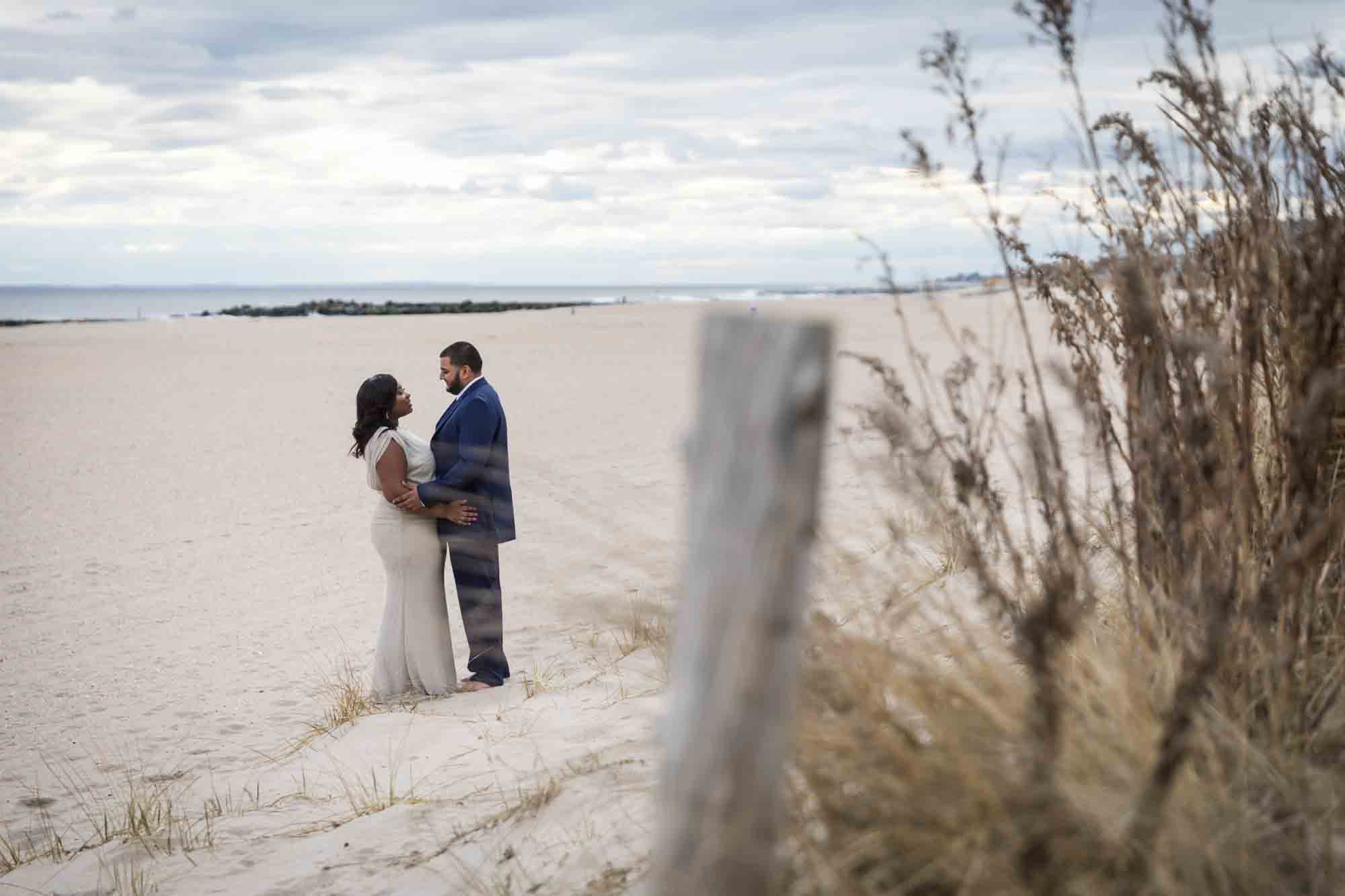 Couple hugging on beach with grass on the side