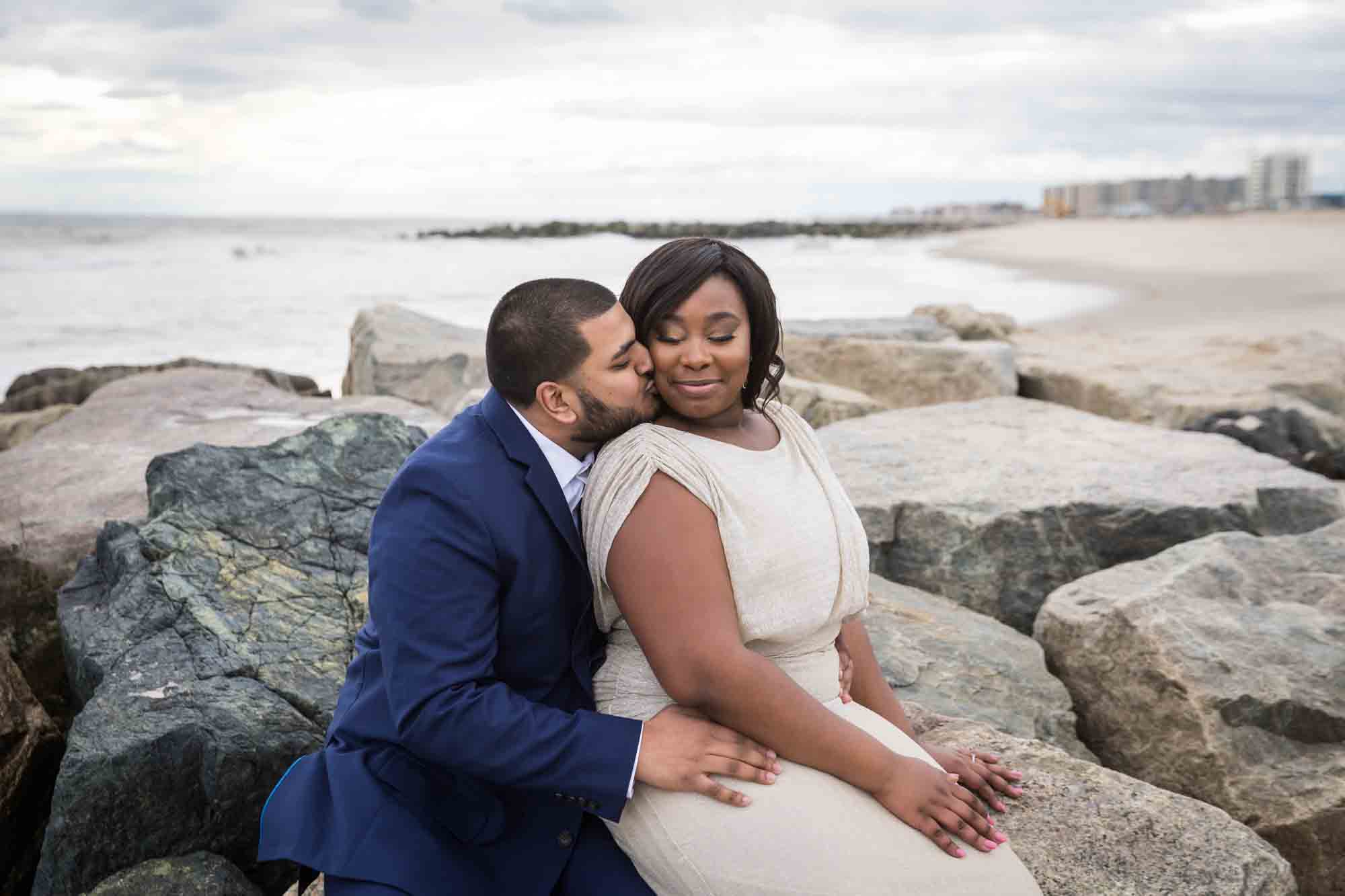 Couple sitting on rock jetty for an article on how to plan the perfect beach engagement photo shoot