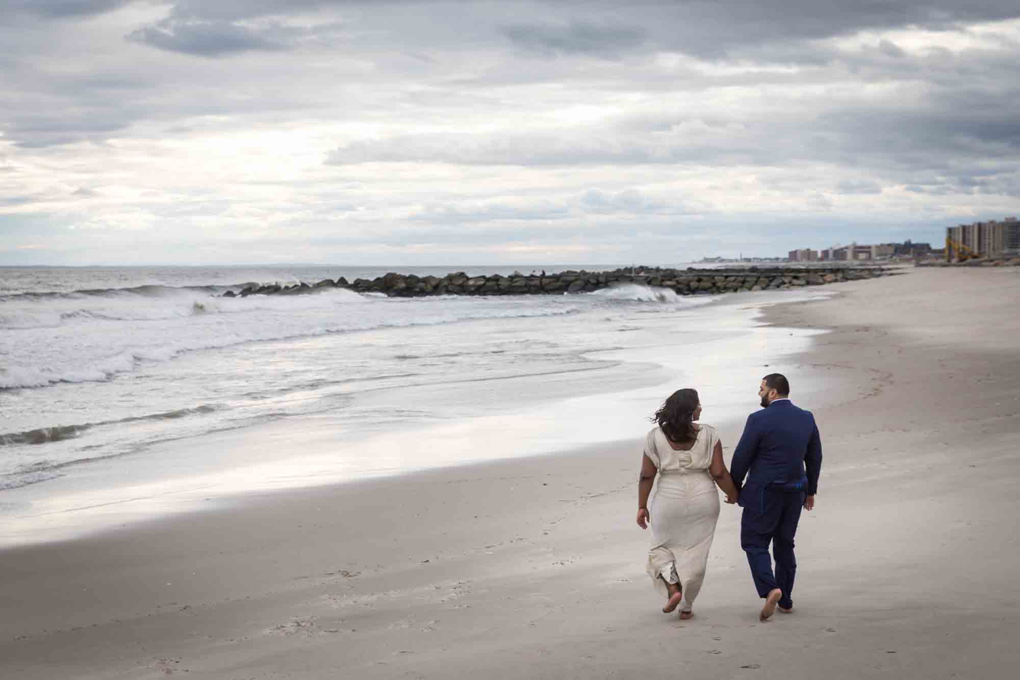 Couple holding hands and walking on beach for an article on how to plan the perfect beach engagement photo shoot