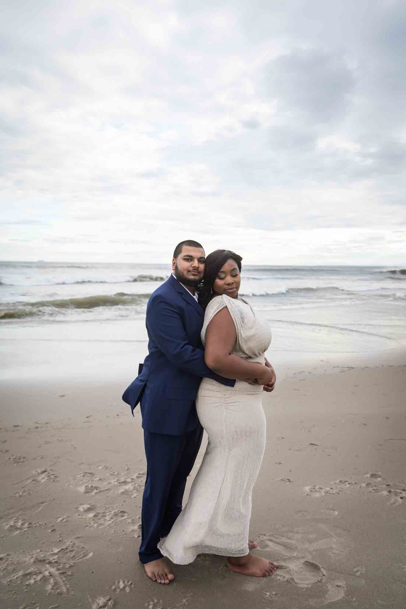 Couple cuddling in front of waves on beach for an article on how to plan the perfect beach engagement photo shoot