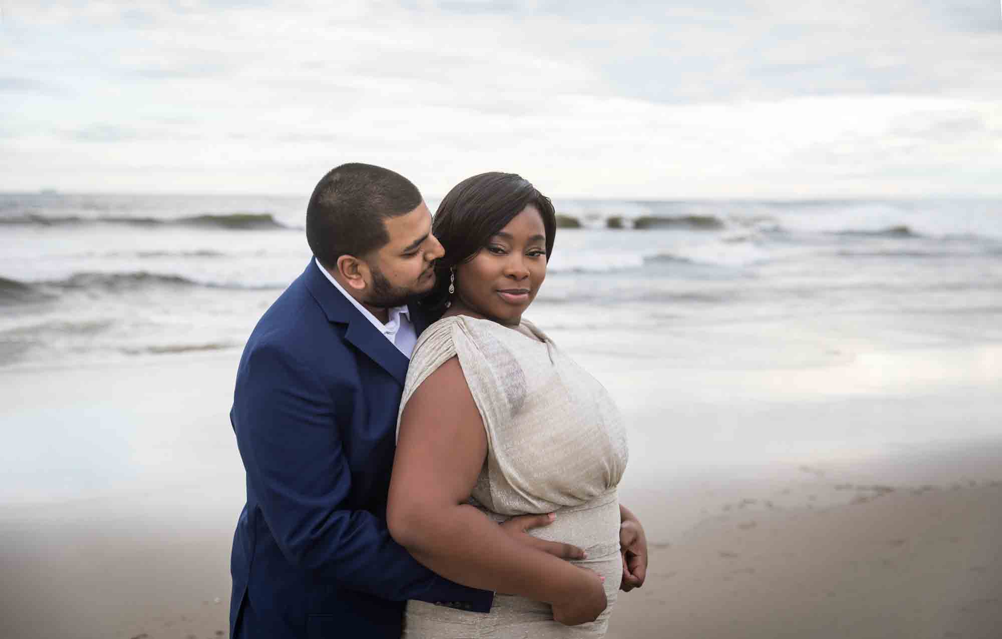 Couple cuddling in front of waves for an article on how to plan the perfect beach engagement photo shoot