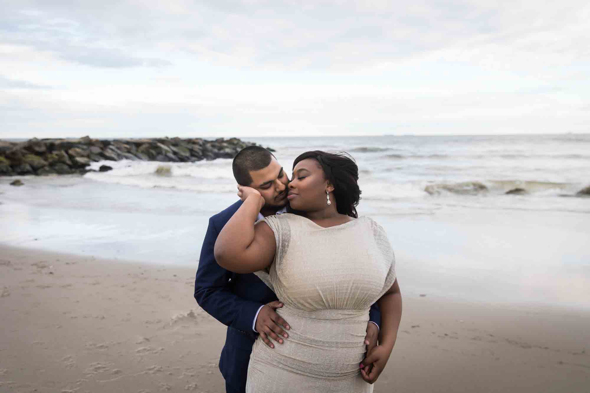 Couple cuddling in front of rock jetty and waves