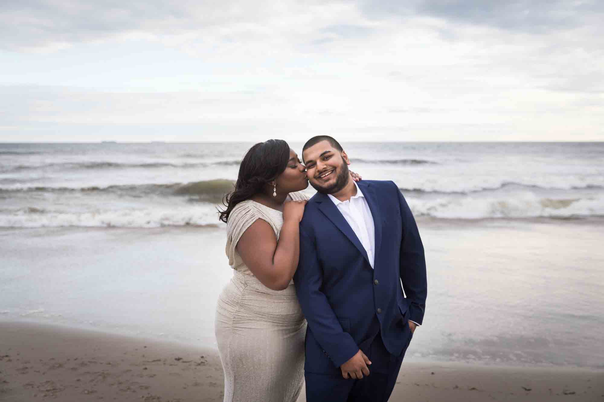 Woman kissing man on the cheek for an article on how to plan the perfect beach engagement photo shoot