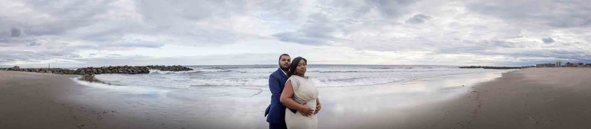 Panoramic view of couple cuddling in front of waves on beach