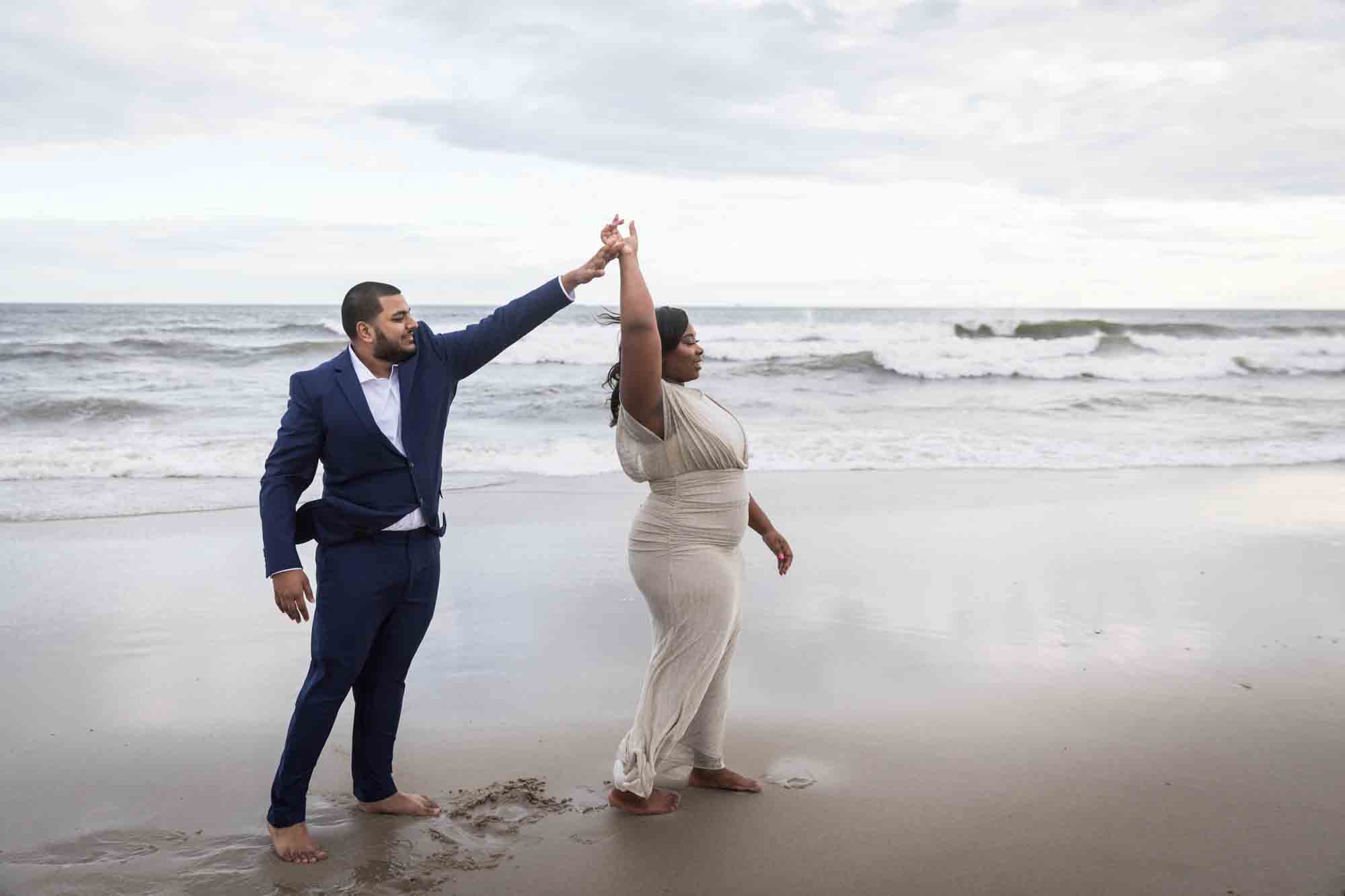 Couple dancing in front of waves for an article on how to plan the perfect beach engagement photo shoot