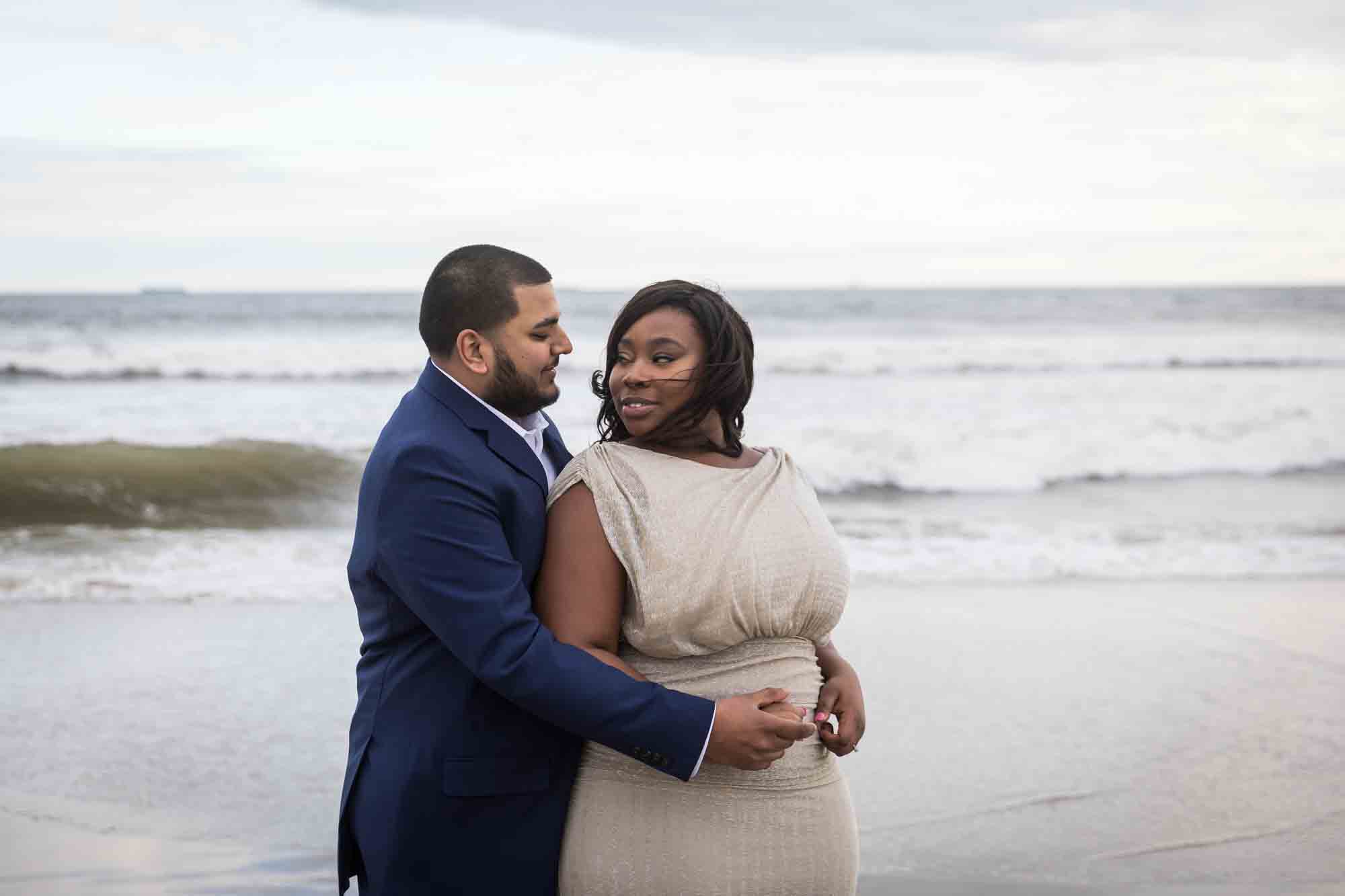 Couple cuddling in front of waves for an article on how to plan the perfect beach engagement photo shoot