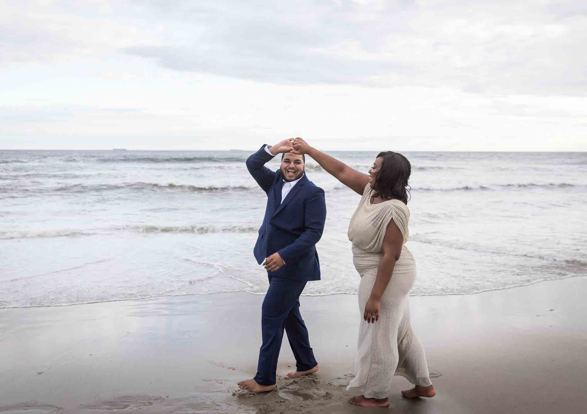 Couple dancing in front of waves for an article on how to plan the perfect beach engagement photo shoot