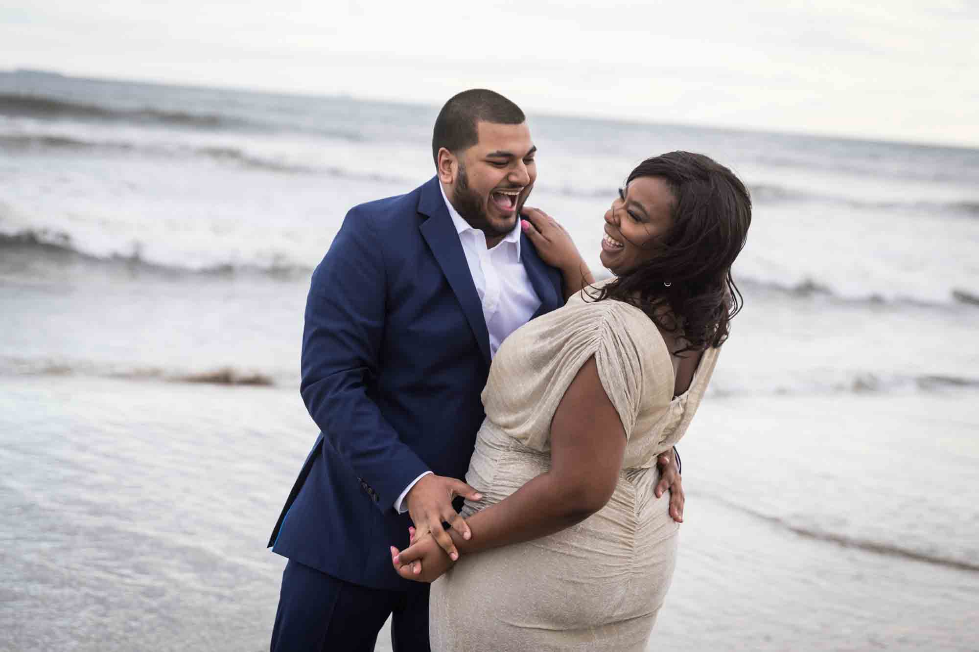 Couple dancing in front of waves for an article on how to plan the perfect beach engagement photo shoot